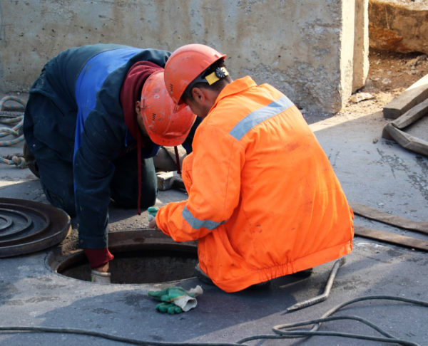Workers,Over,The,Open,Sewer,Hatch,On,A,Street.,Concept